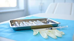 В металлическом подносе лежат ампулы, рядом лежит шприц и перчатка